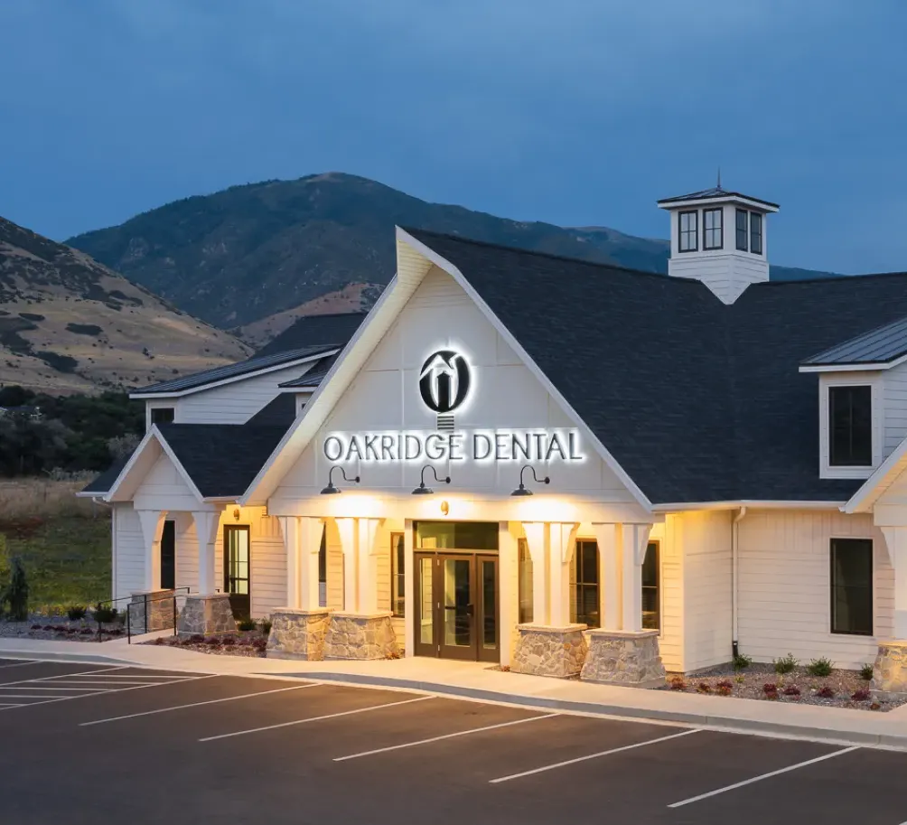Oakridge Dental's farmhouse-style office in Farmington at dusk, with the mountains behind it